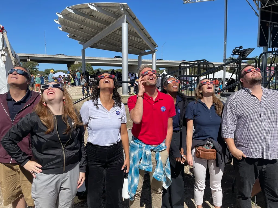 A group of people wearing eclipse glasses stare up at the sky.